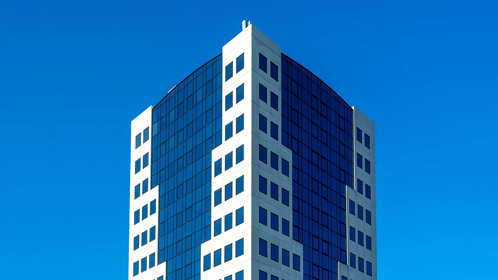 Modern high-rise commercial office building with reflective glass facade under a bright blue sky