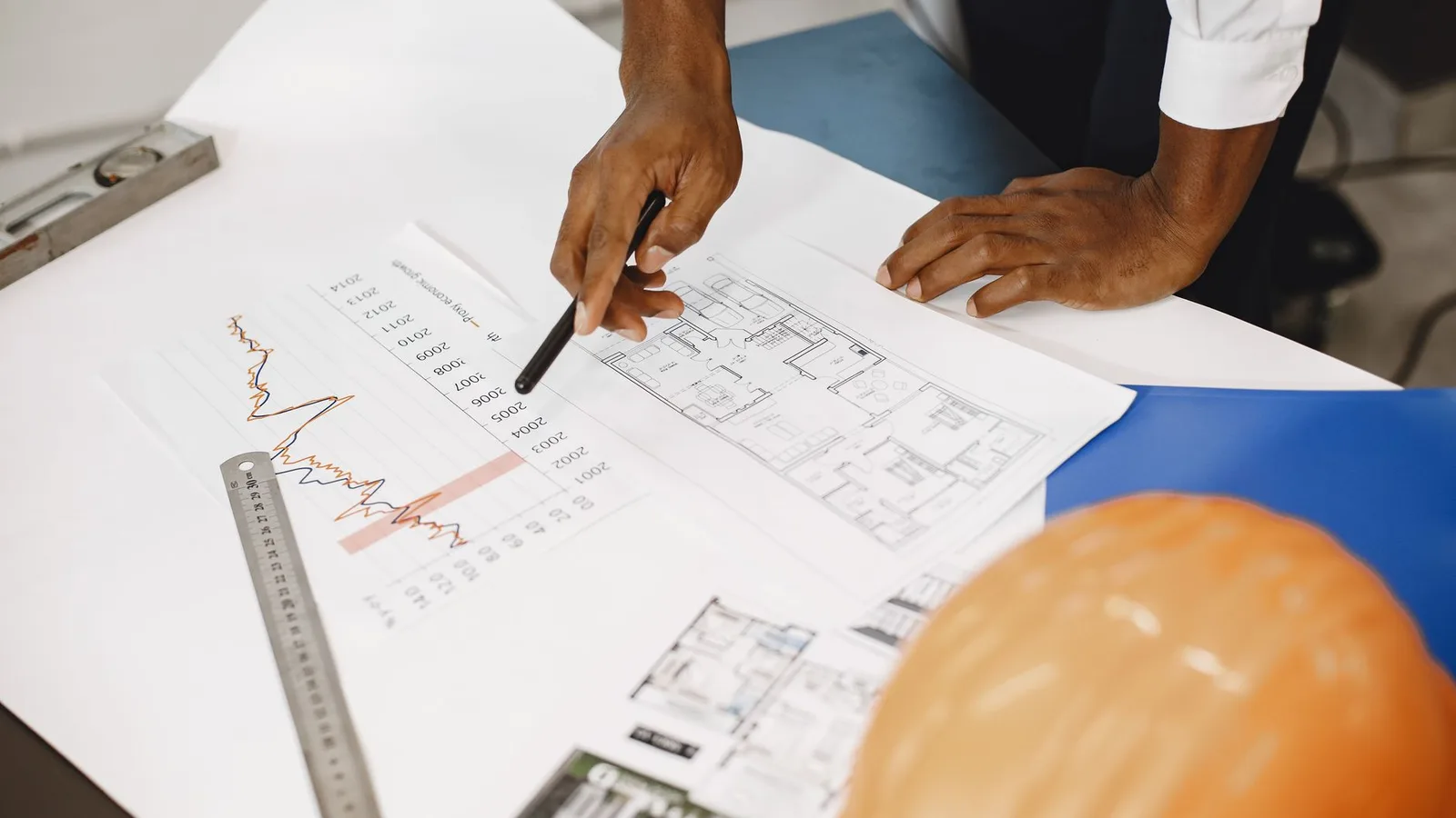 Hands of an architect analyzing blueprints and financial graphs at a desk