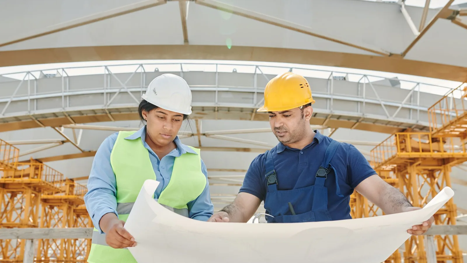 Male and female engineers discussing blueprints at a construction site, promoting teamwork and planning
