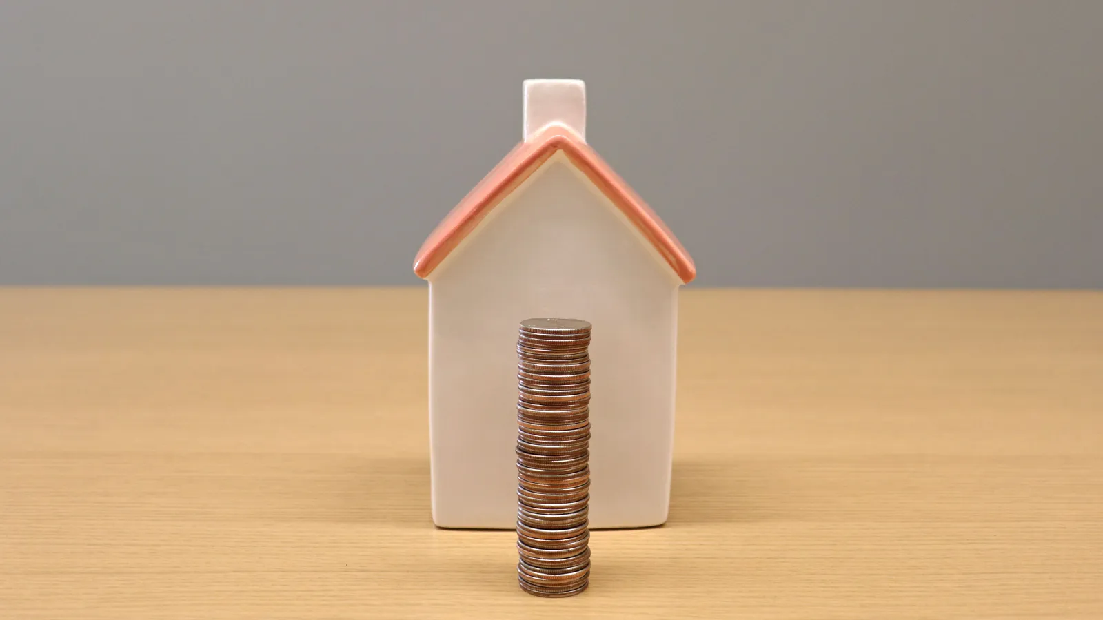 Stack of coins beside a model house, representing loan-to-value ratio and deposit on a commercial property loan