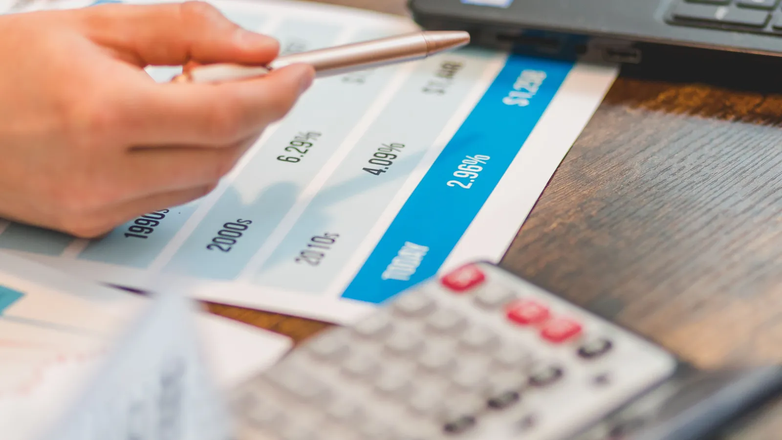 Hand pointing a pen at a chart of historical interest rate percentages beside a calculator