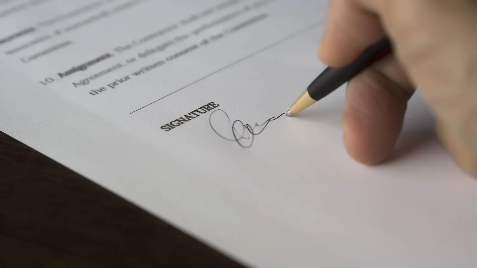 A hand signs a formal contract with a pen on a wooden desk, symbolizing the final execution of equipment financing