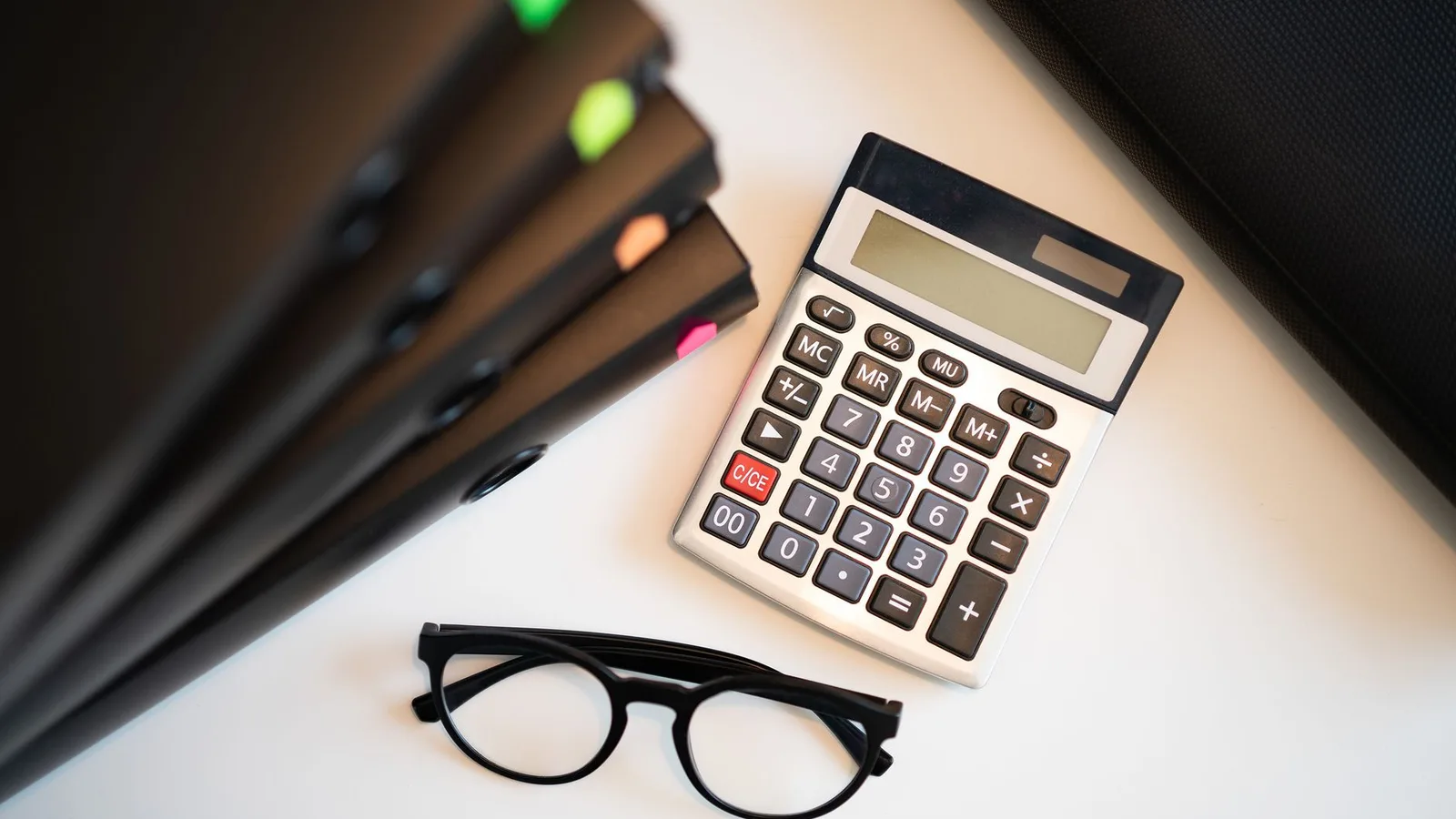 Calculator with glasses and folders on an office desk, representing the pricing and terms of equipment financing