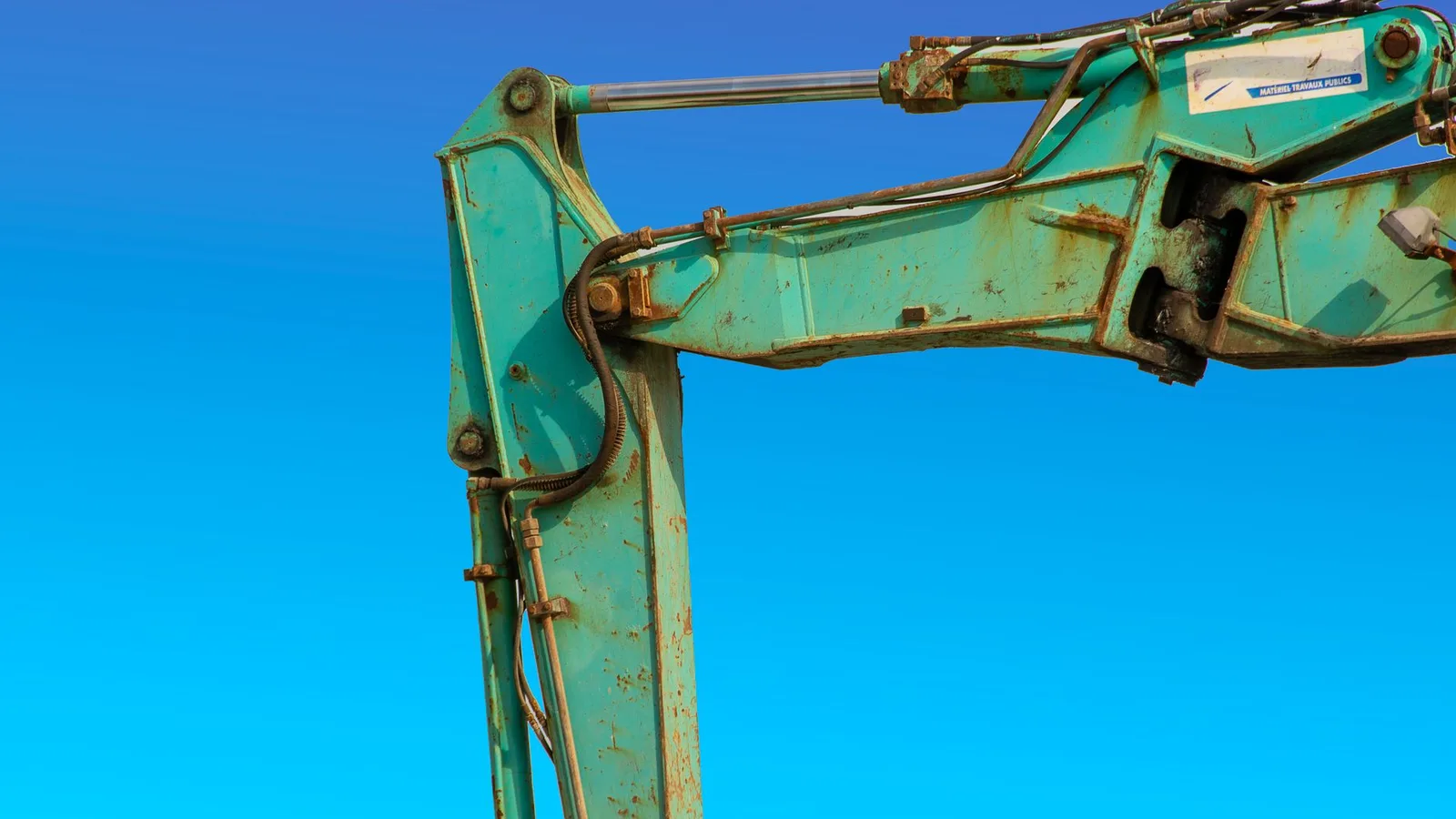 Detailed view of a turquoise excavator arm against a vivid blue sky, representing heavy machinery funded through equipment financing