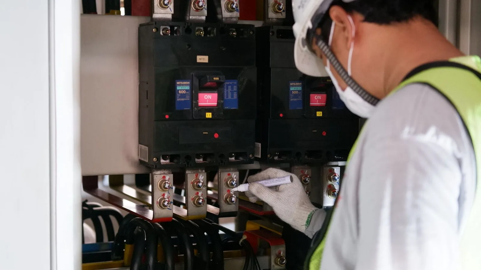 Technician wearing safety gear inspecting electrical panels in an industrial setting, showing equipment inspection