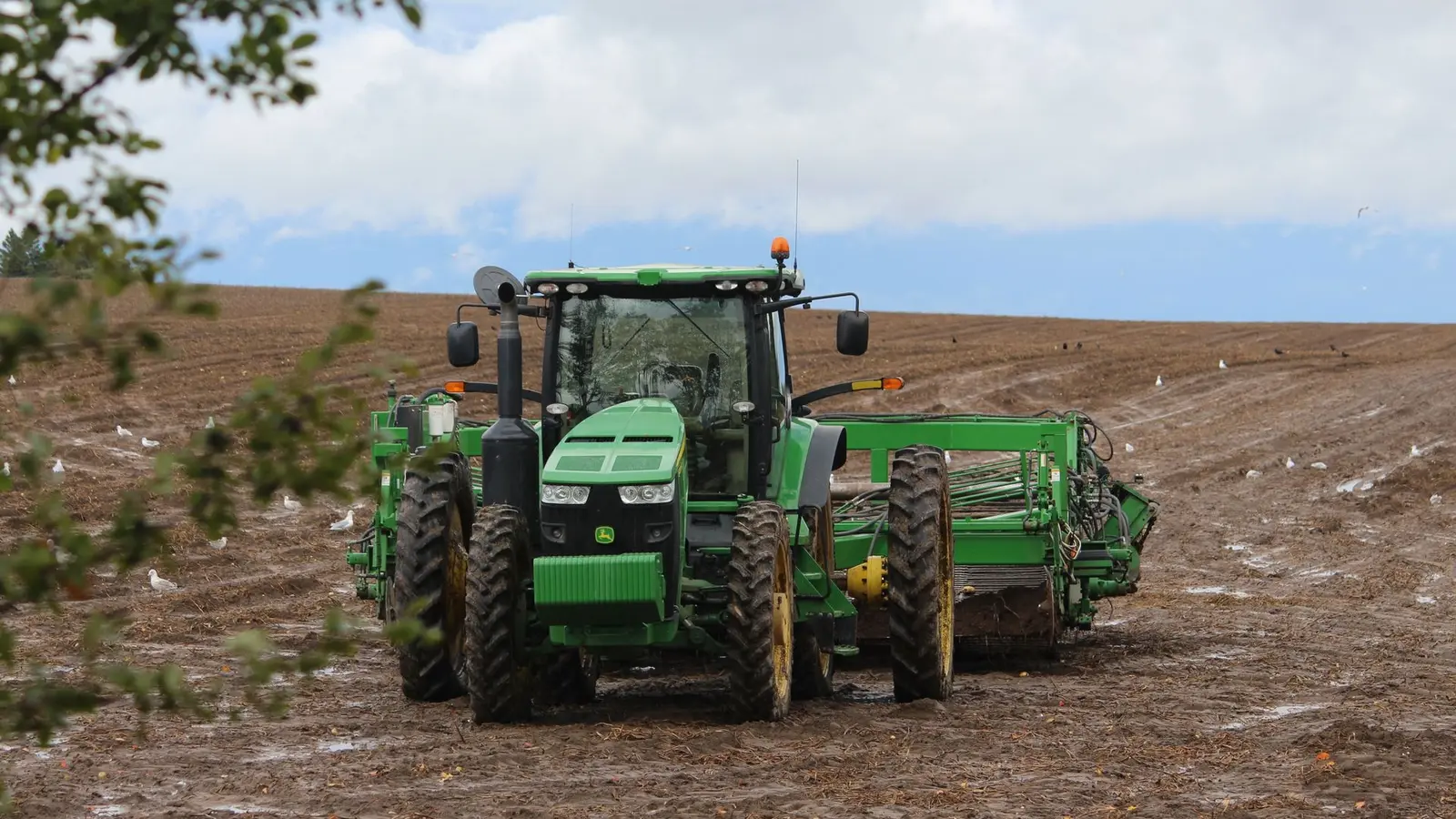 Green tractor working a plowed field under a cloudy sky
