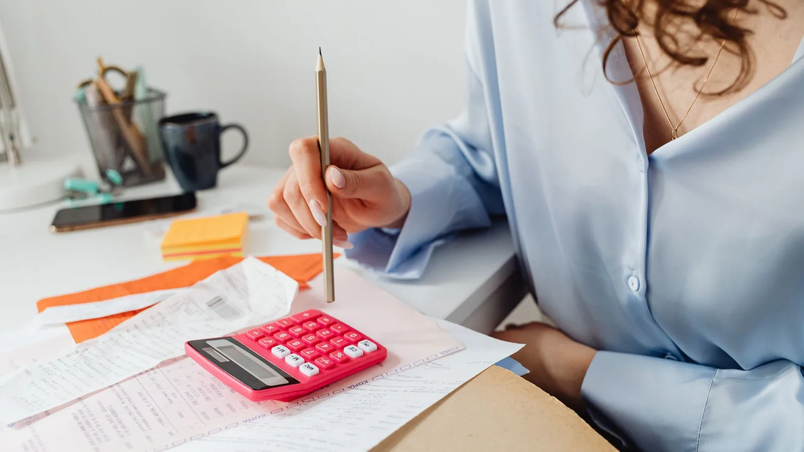 A woman calculating business expenses using a calculator and financial invoices at her desk in New Zealand