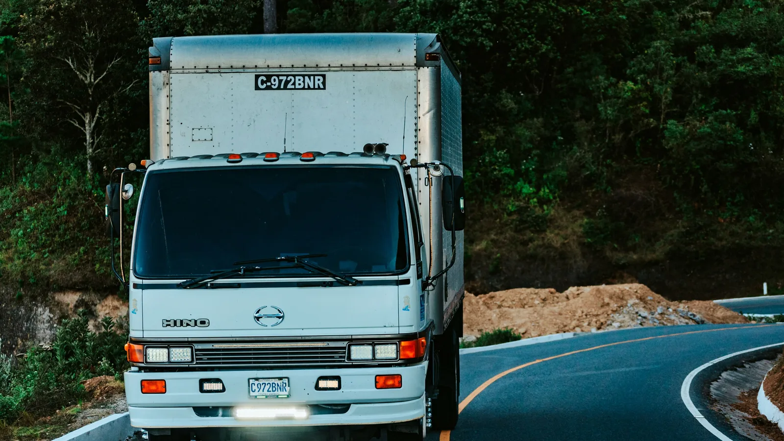 Commercial heavy transport truck navigating a winding highway through dense green forest in New Zealand