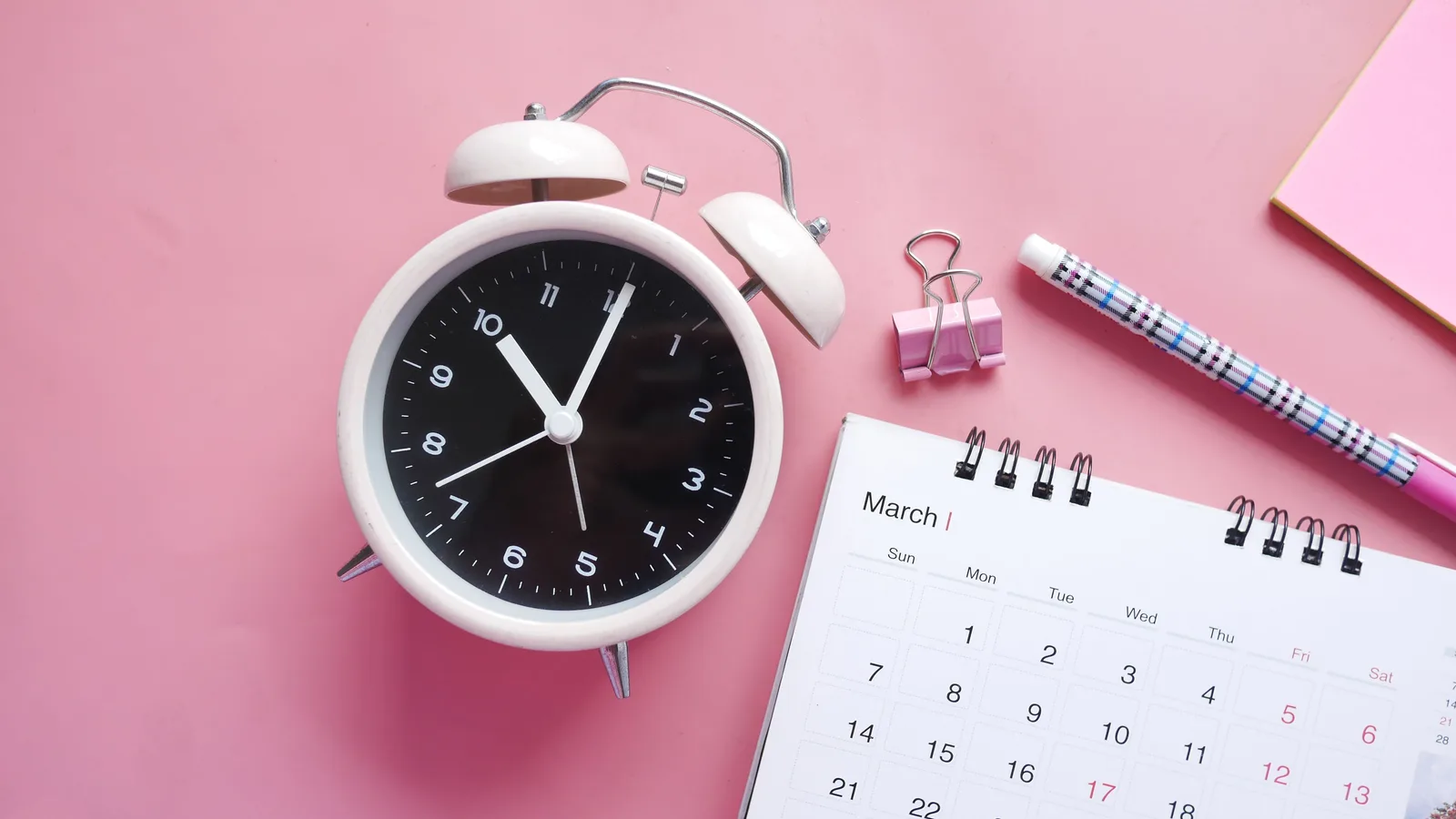 Alarm clock beside a desk calendar, representing the 12-month trading history mainstream banks require from self-employed borrowers