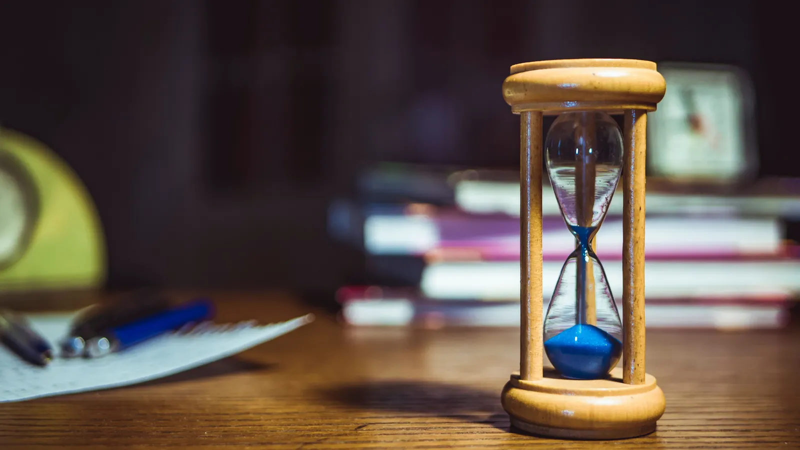 Wooden hourglass on a desk beside books and papers, representing the fixed timeframe of a short-term business loan