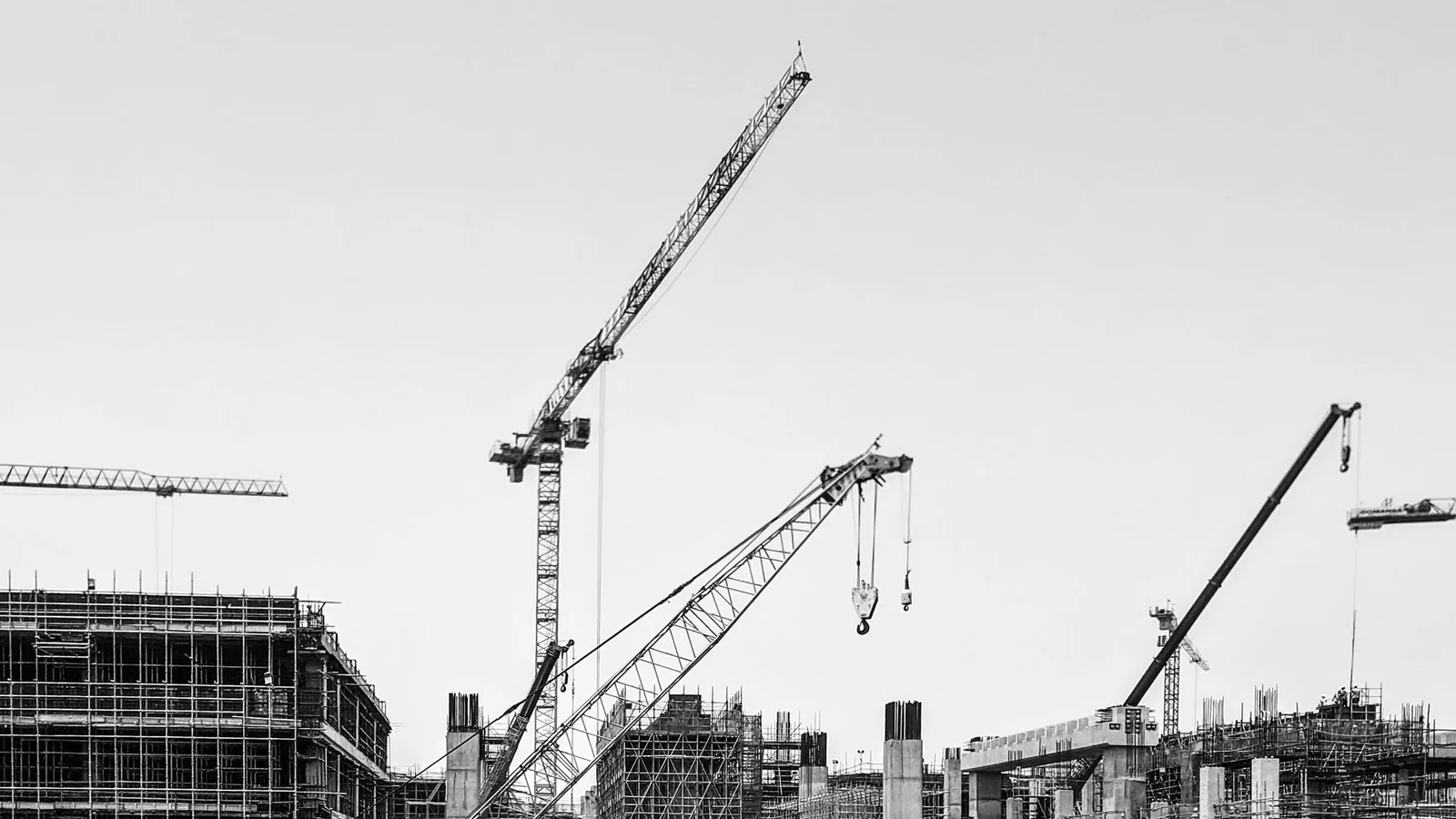 Black and white image of cranes working on a large construction site under a clear sky.