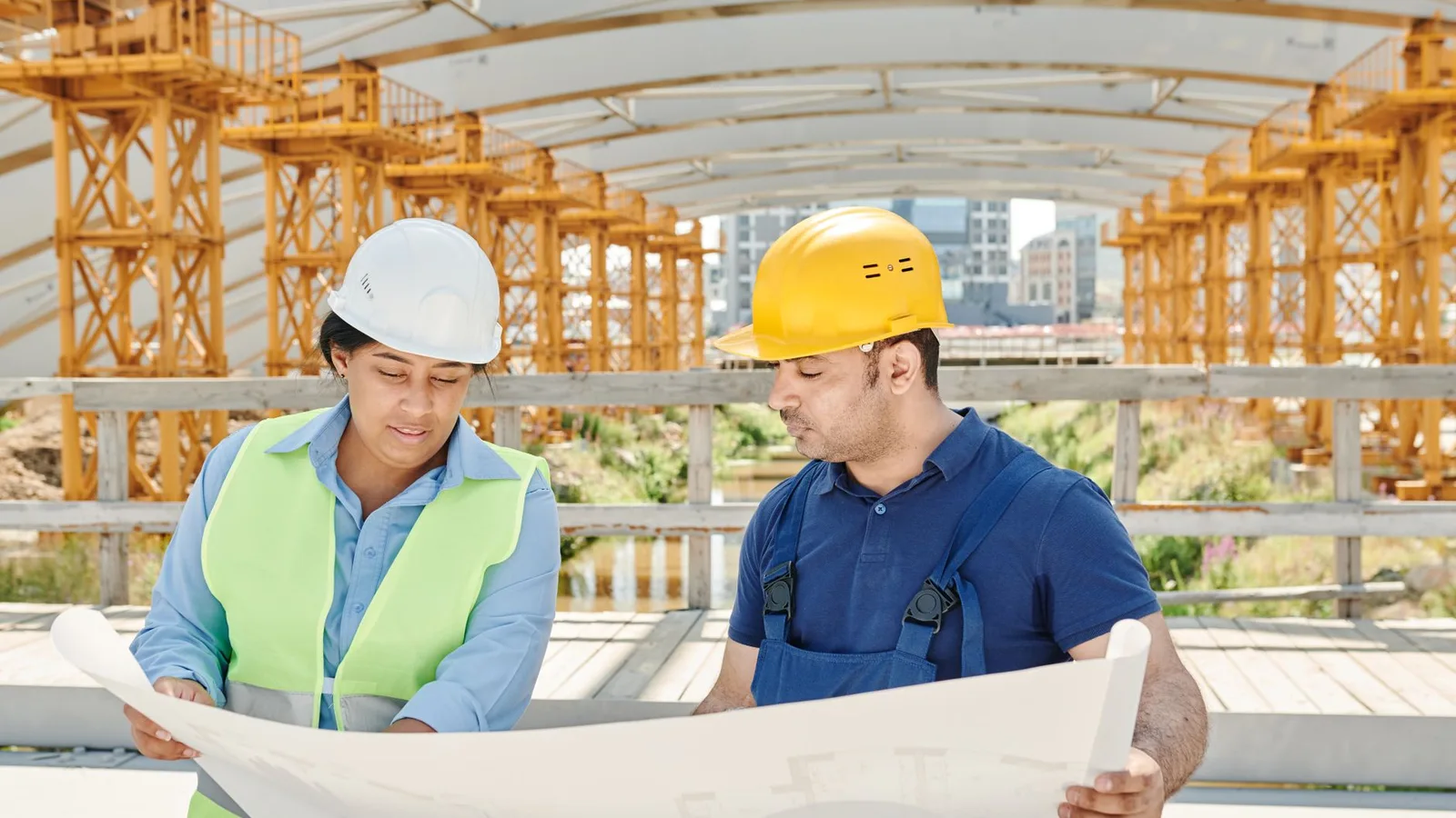 Engineering team analyzing blueprints together at an outdoor construction site with safety gear.