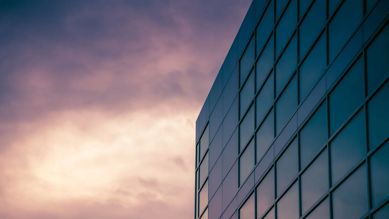 A sleek modern skyscraper reflecting the colorful twilight sky, emphasizing urban architecture.