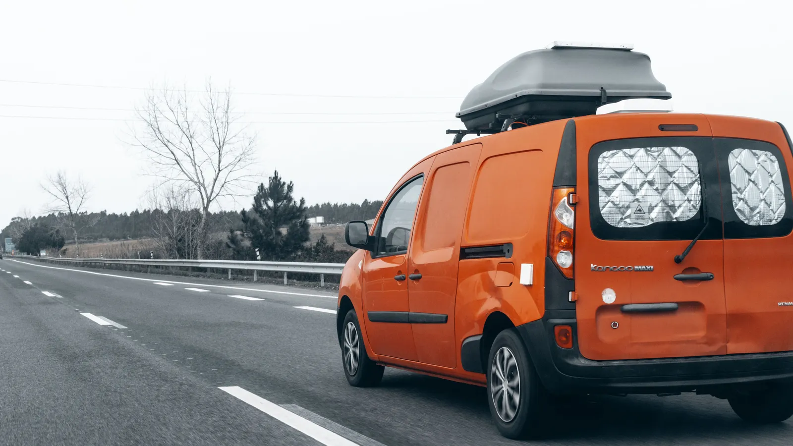 Bright orange work van travelling along an open New Zealand highway with a roof box fitted, the type of vehicle funded through van finance