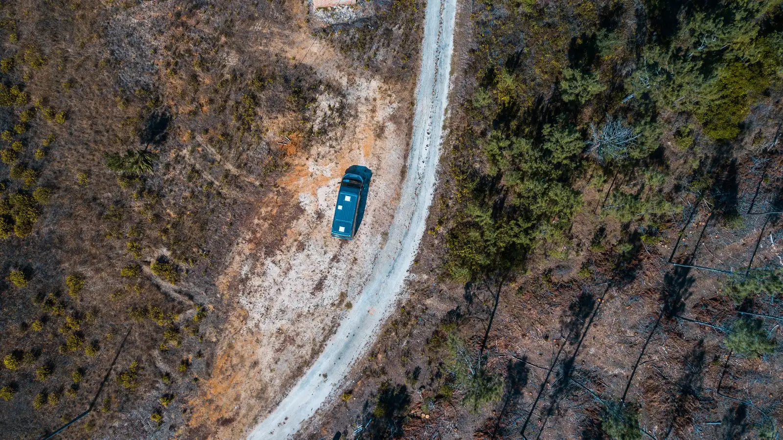 Campervan parked on a rural New Zealand dirt road surrounded by trees and fields, seen from above
